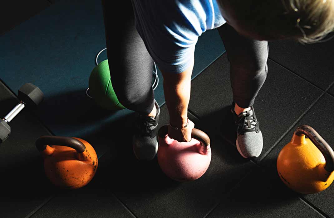 A fitness enthusiast carrying a pink kettlebell with other weights and kettlebells around them on the floor