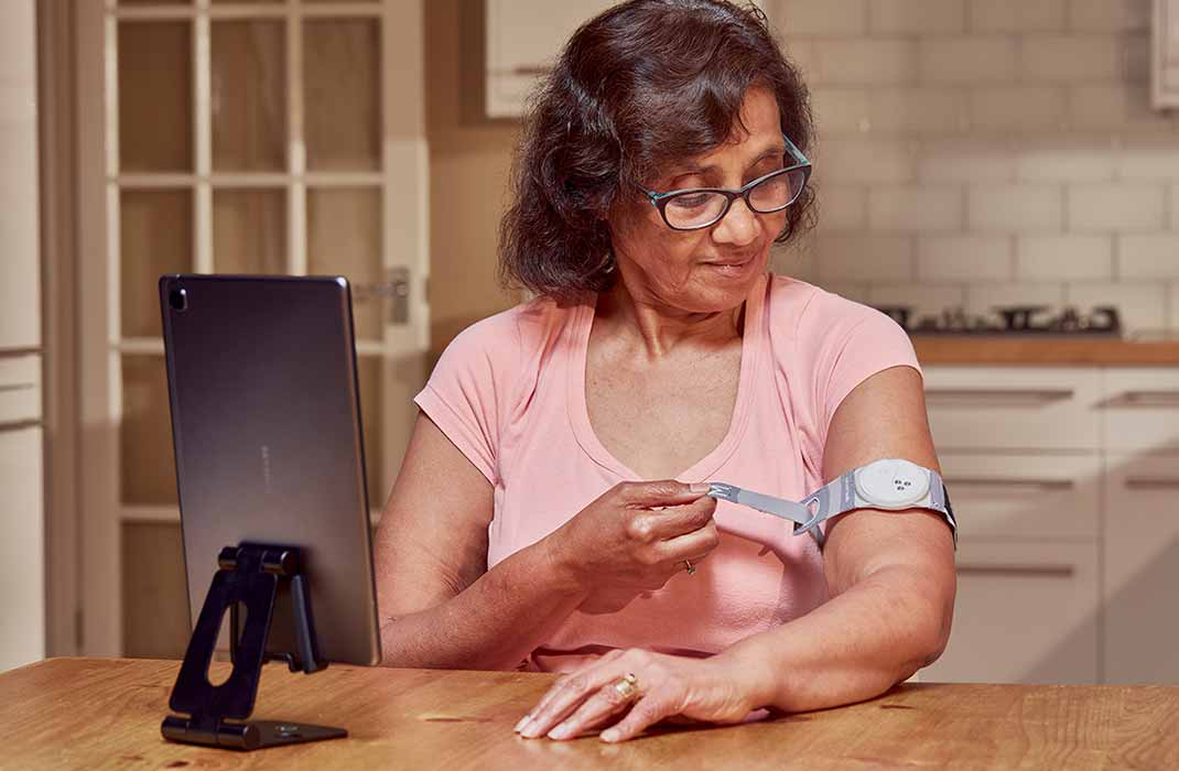 woman at home applying a wearable medical device to arm