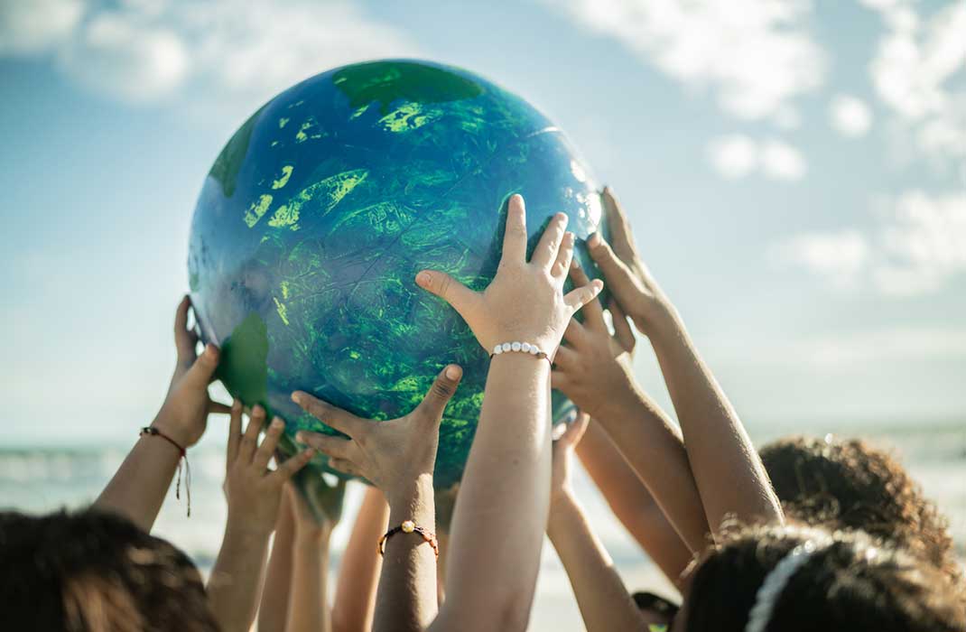 Children's hands holding up a globe at the seaside.