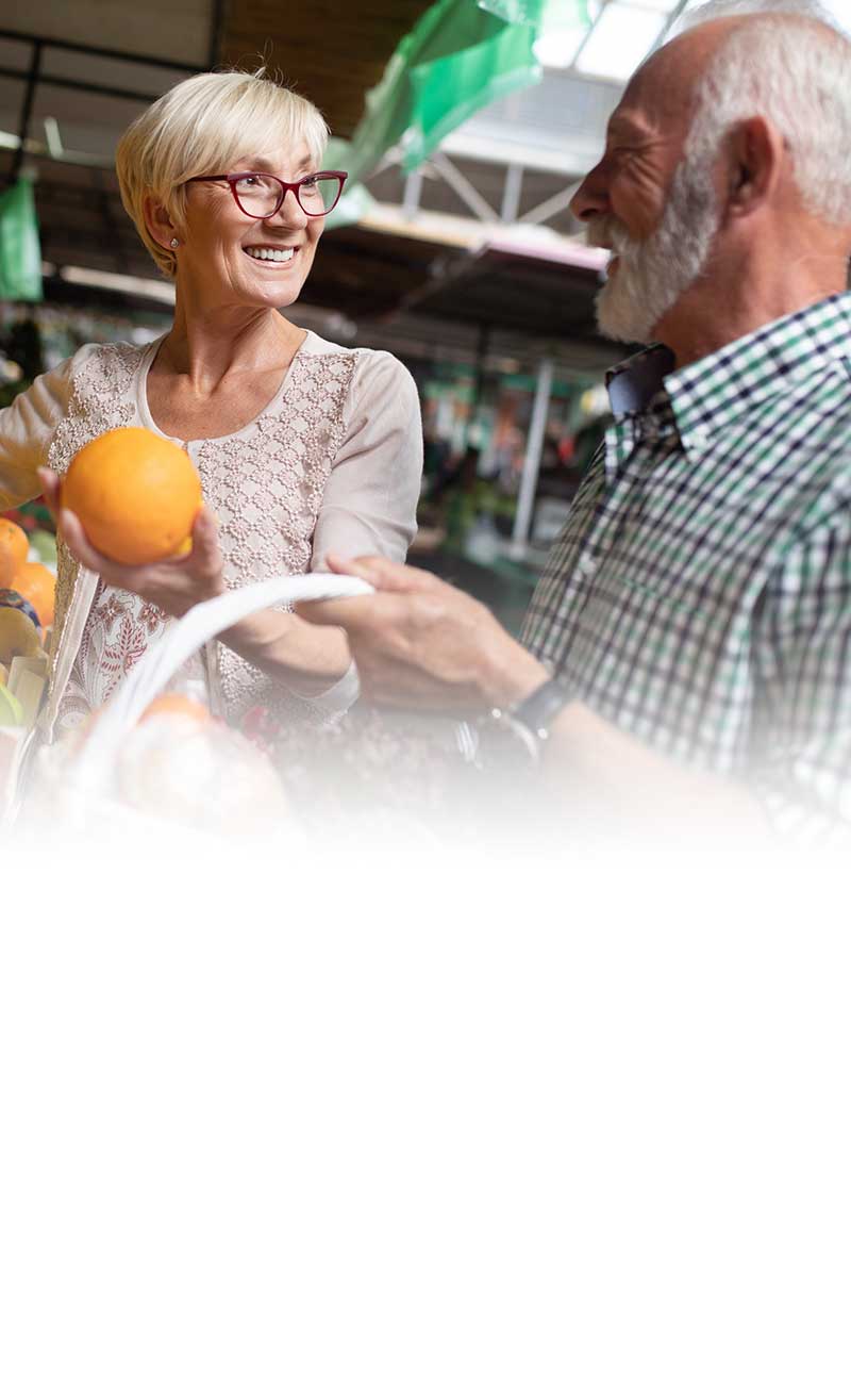 man and woman smiling while picking oranges at grocery store