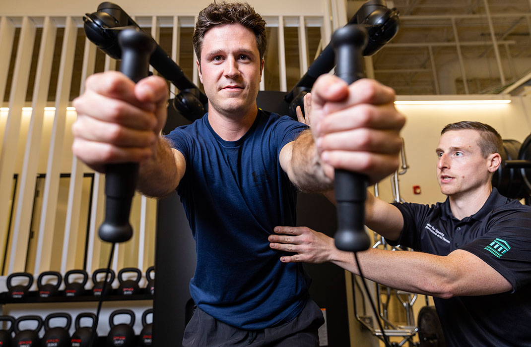 athletic trainer supervising male client on weighted row machine in gym