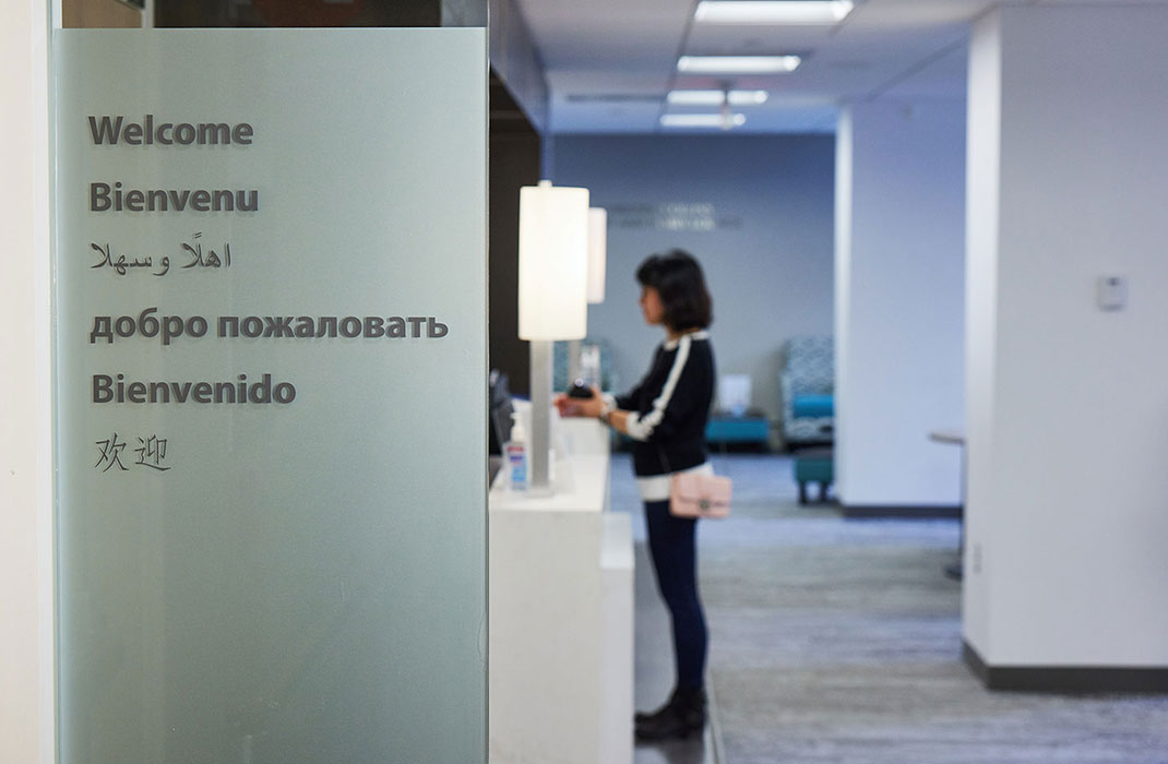 A welcome sign in several languages, with the clinic visible through the glass wall.
