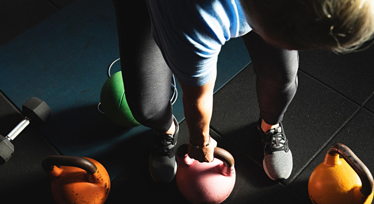 A fitness enthusiast carrying a pink kettlebell with other weights and kettlebells around them on the floor