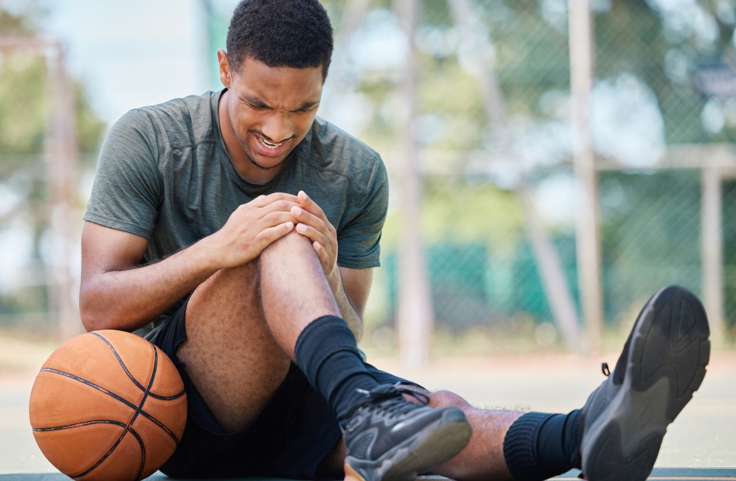 A black man holding his knee from a basketball injury.