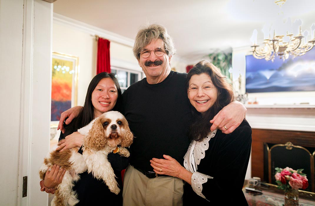Three people standing together and smiling while one of them is holding a dog