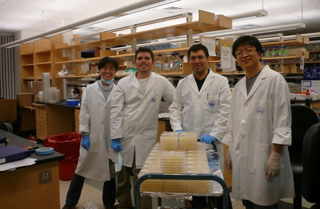 Four research lab members smiling and standing with materials in a research lab