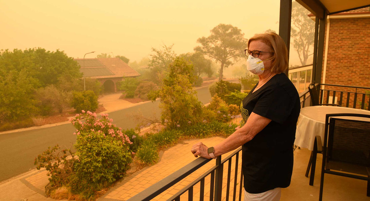 Woman standing on balcony, wearing mask to protect from effects of air pollution all around in the background causing a yellow tint in the area.