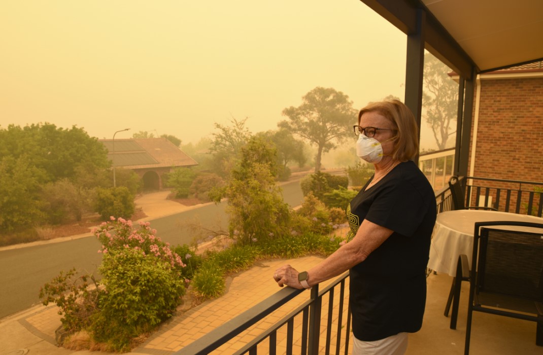 Woman standing on balcony, wearing mask to protect from effects of air pollution.