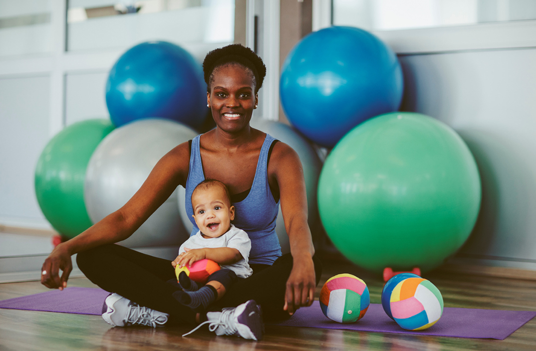A postpartum athlete sitting in a gym with her baby.