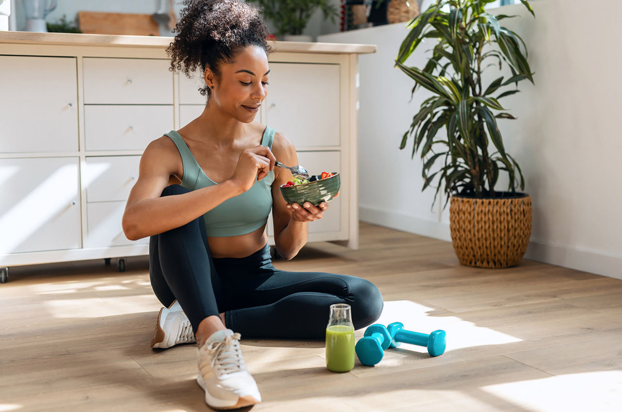 Athletic young woman eats fruit and exercises at home.