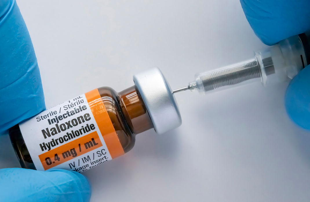 A vial of naloxone that someone is drawing a dose from.