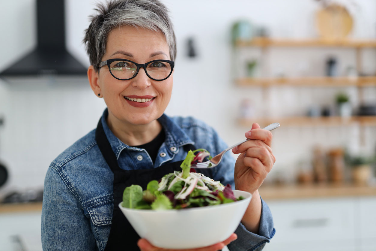 A chic older woman eats a large green salad.