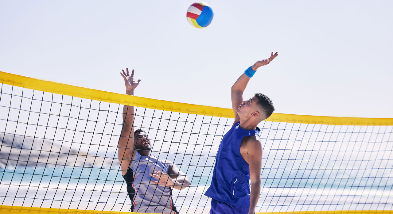 A man using his vertical jump to spike a volleyball.