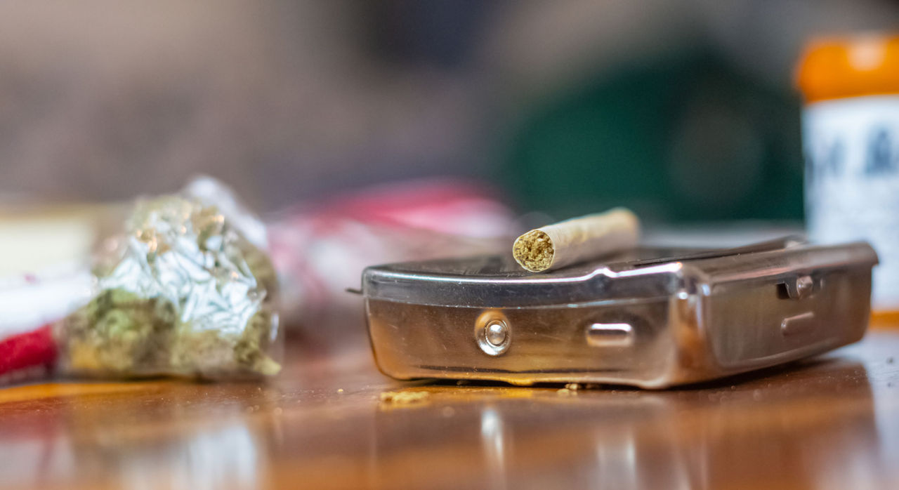 A marijuana joint lying on a tin, with a small bag of marijuana in the background.