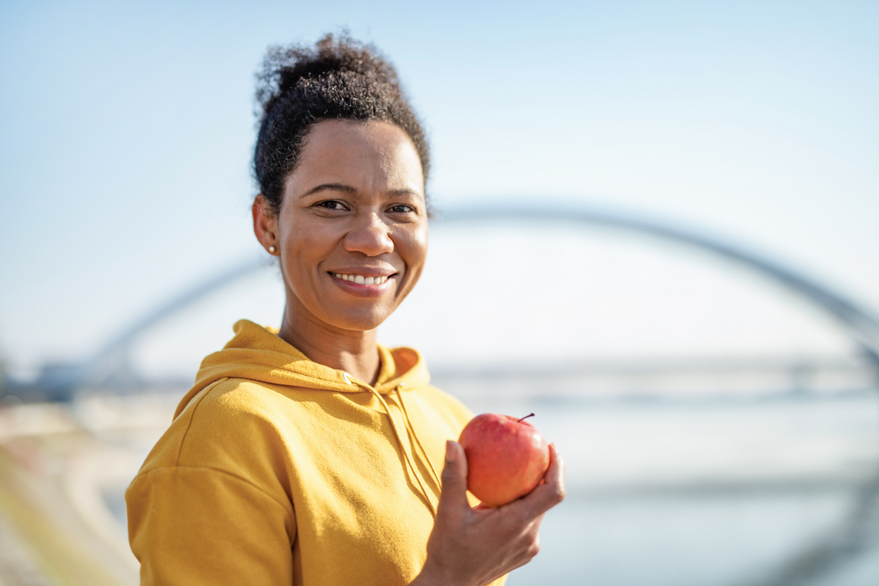 Sporty African American woman eating an Apple outdoors, after exercise.