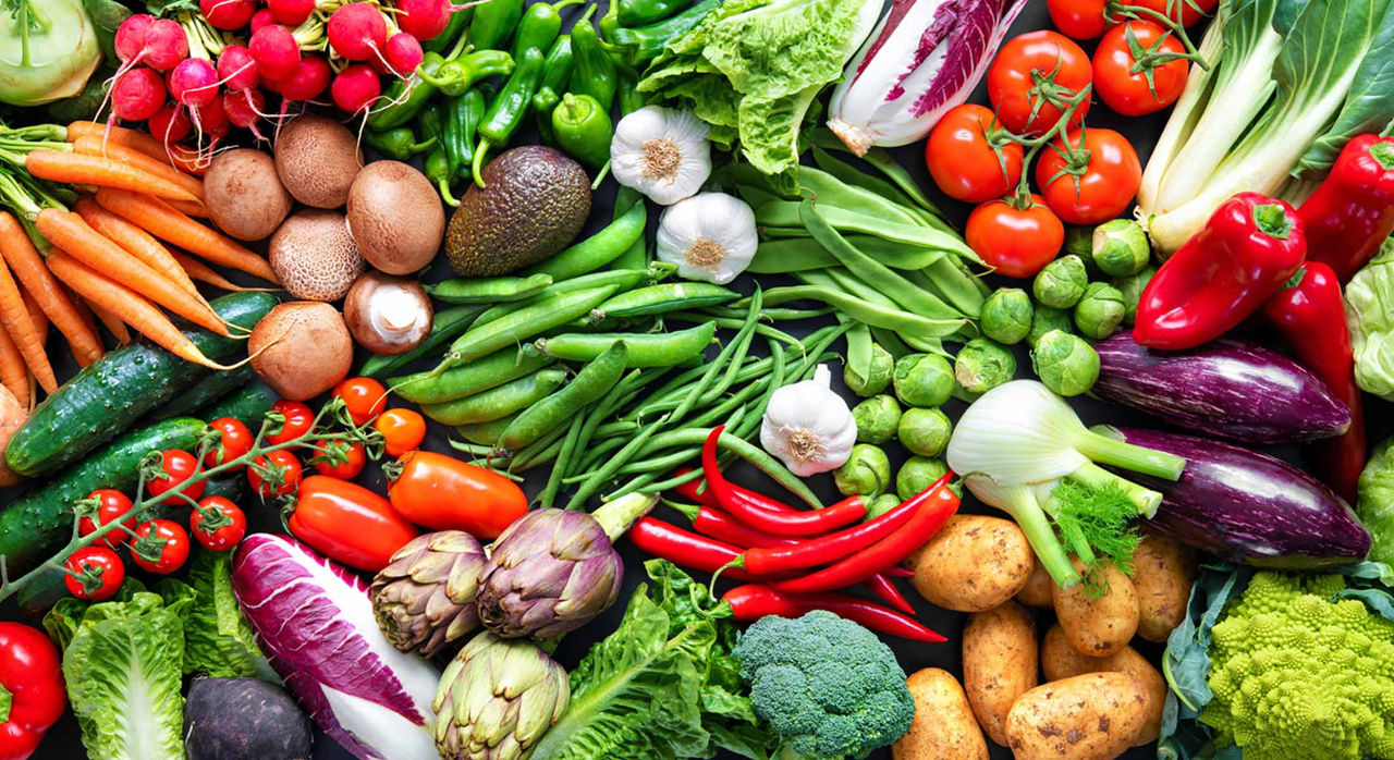 An array of vegetables and ingredients like carrots, tomatoes, Brussels sprouts, potatoes, broccoli, purple cabbage, lettuce, red chiles, radishes, artichokes, and more.