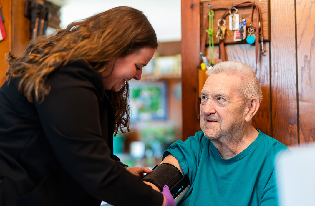 A home health nurse puts a blood pressure cuff on an elderly man at his home.