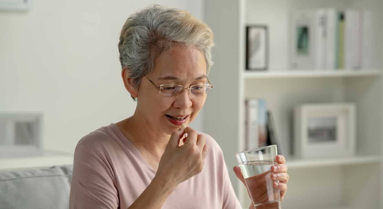 An older Asian woman takes a pill with a glass of water.