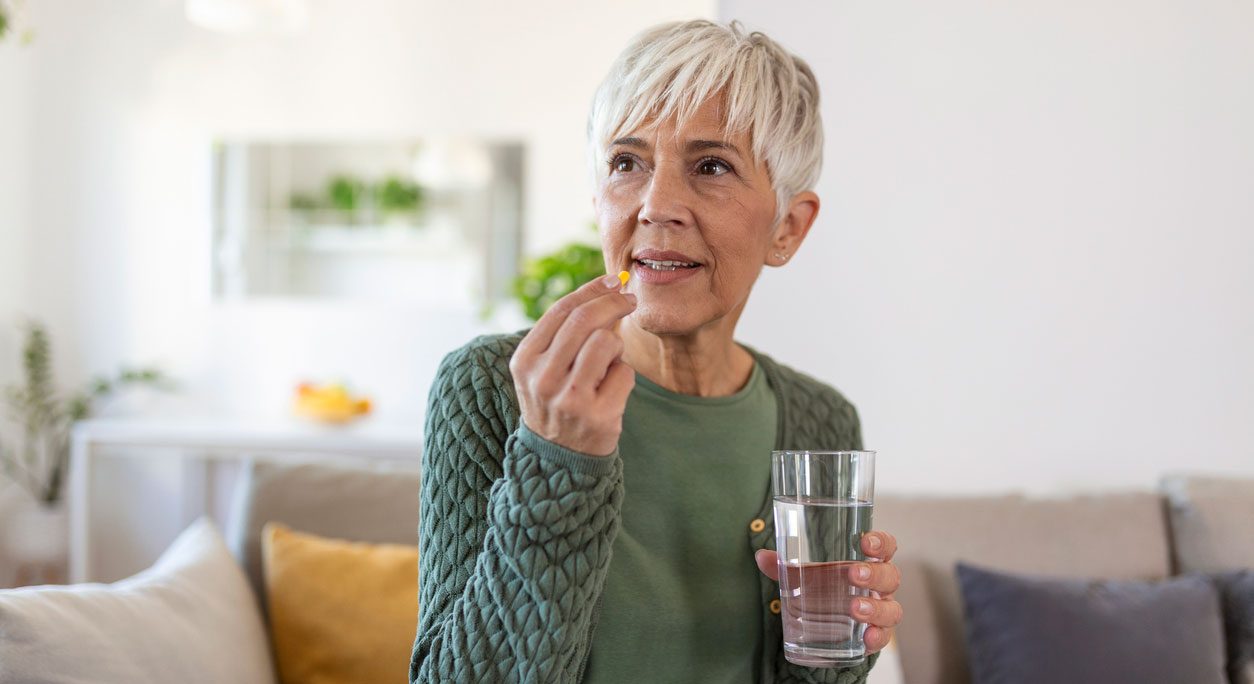 An older woman takes a pill with a glass of water.
