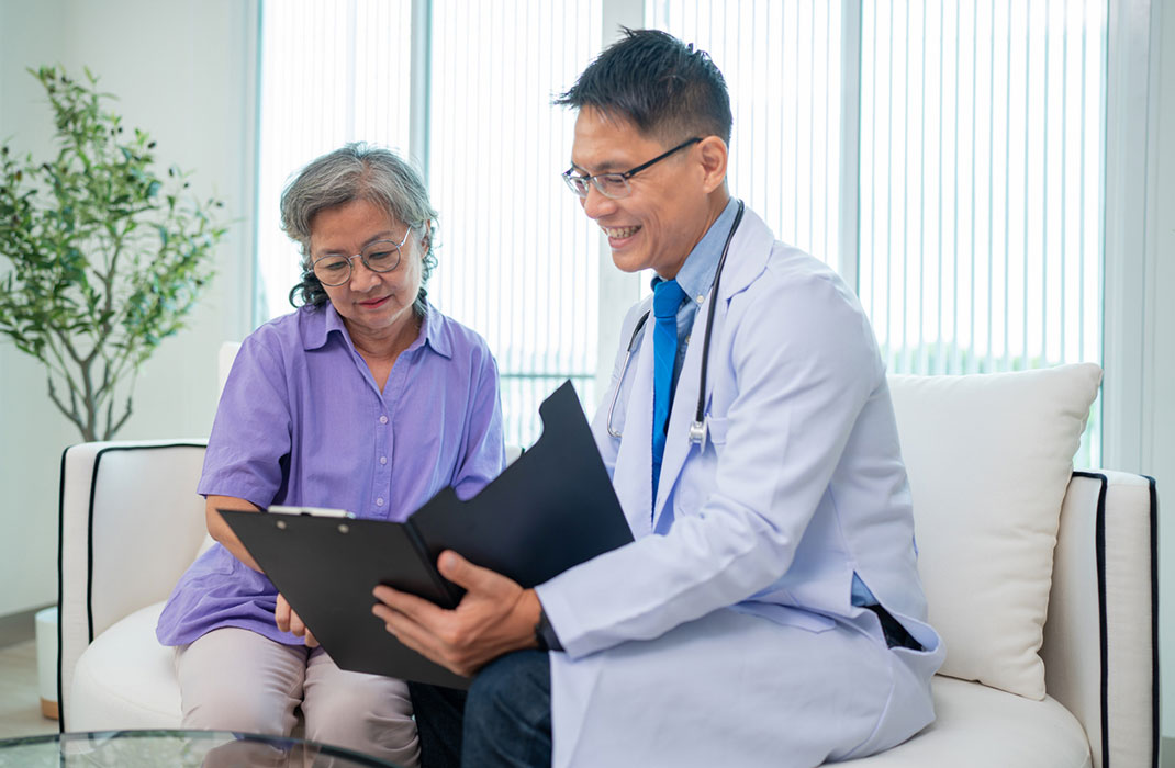 A smiling doctor shows a clipboard with positive results to an older female patient. 