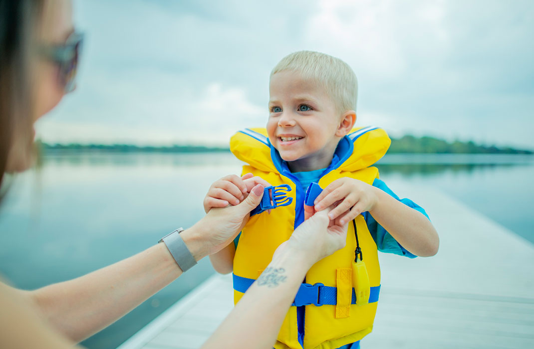 A child at the lake wears a life vest to prevent drowning.