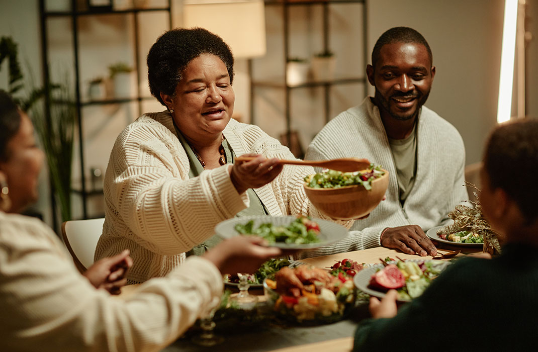 2086769191 Portrait of smiling African-American grandmother serving food while celebrating Thanksgiving with big happy family at dinner table