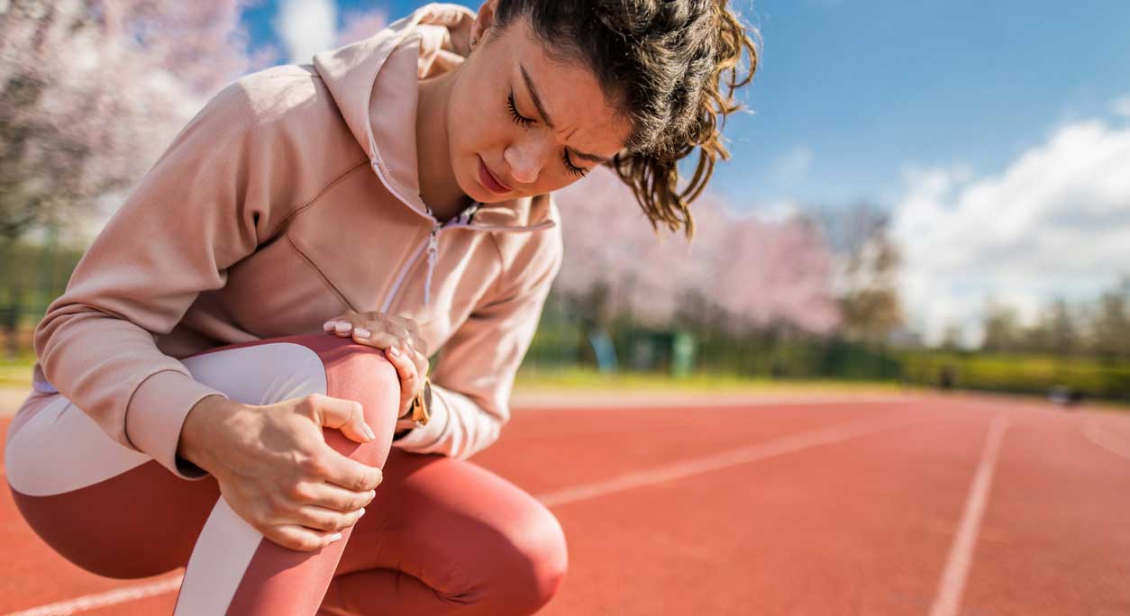A young woman kneels on a running track, holding her knee.