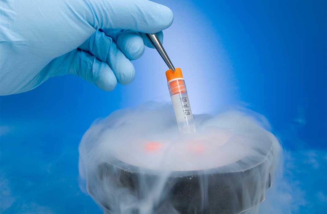 A gloved hand lowers a vial into a container of dry ice.