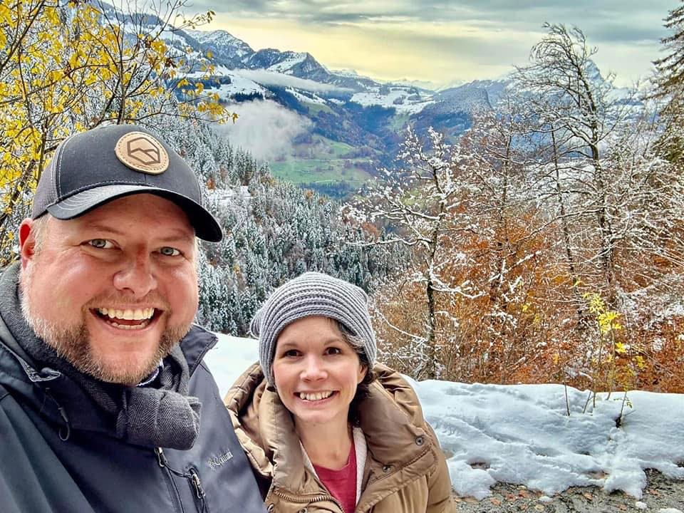 Jenn and her husband on a mountainside, with a stunning view of the Swiss Alps in the background.