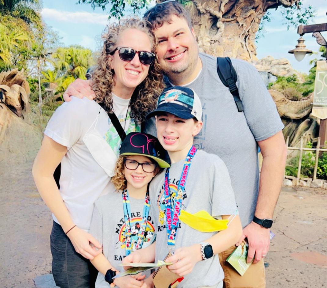 A mother and father smiling and hugging two of their kids who are wearing caps and smiling