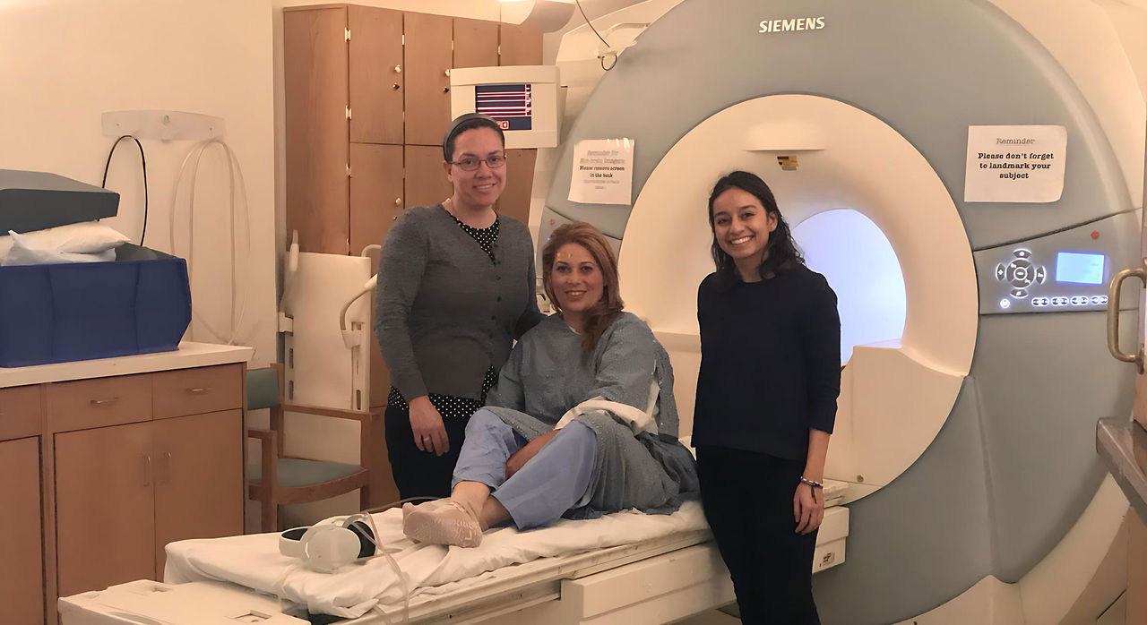 Two practitioners flanking a smiling woman sitting on an MRI bed.