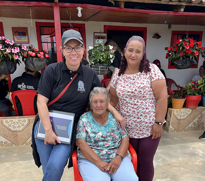 Two older Colombian women and a researcher in the flower-filled courtyard of the women's house.