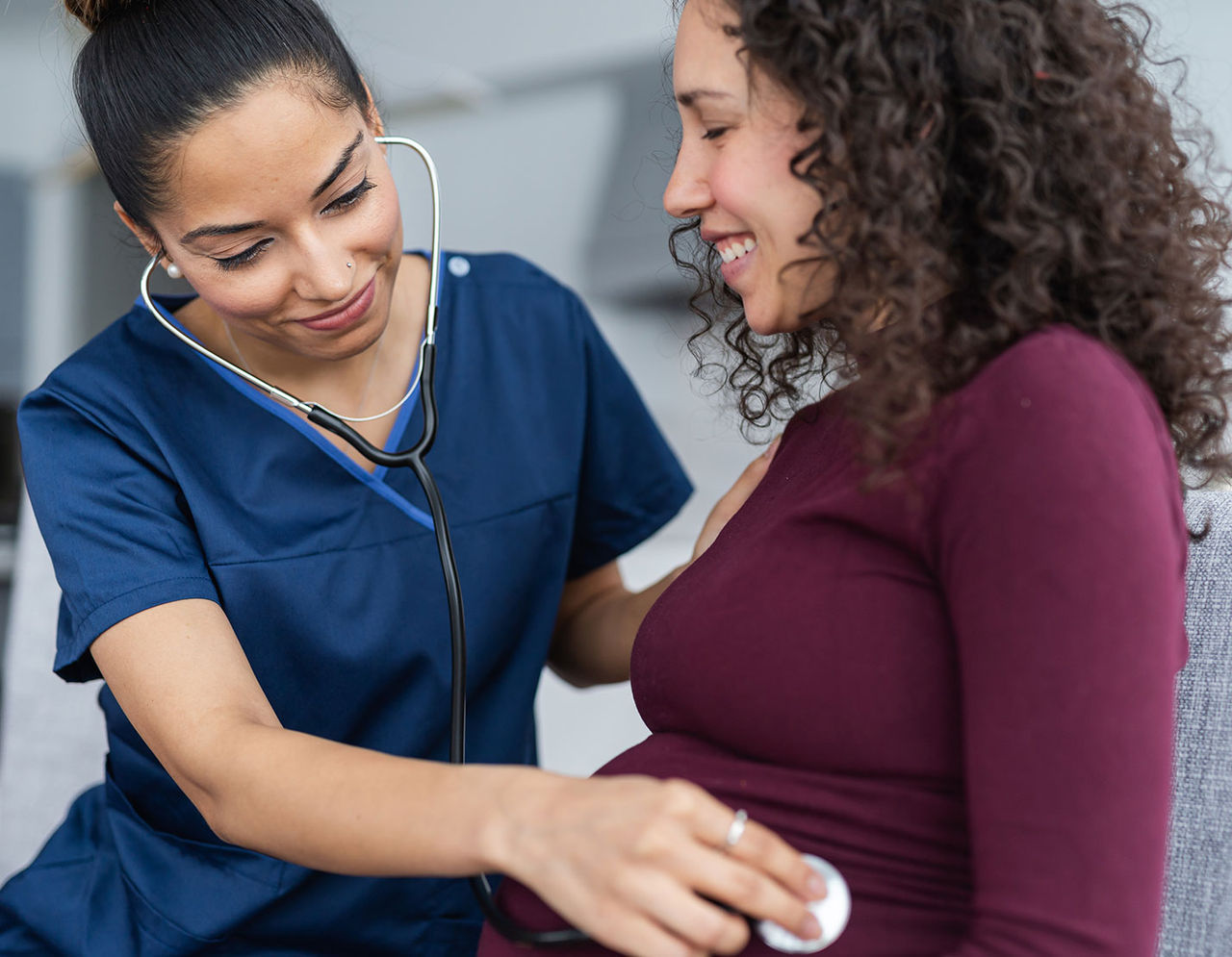 A nurse listens to a pregnant woman's stomach with a stethoscope.
