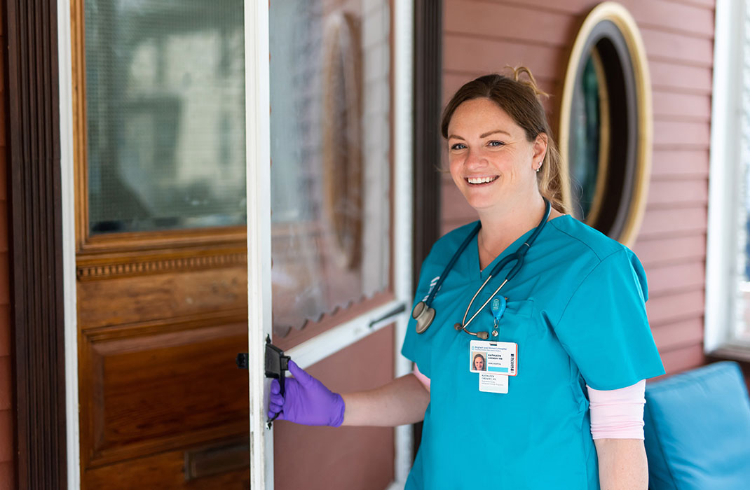 female provider in scrubs smiling and opening door to patient's home