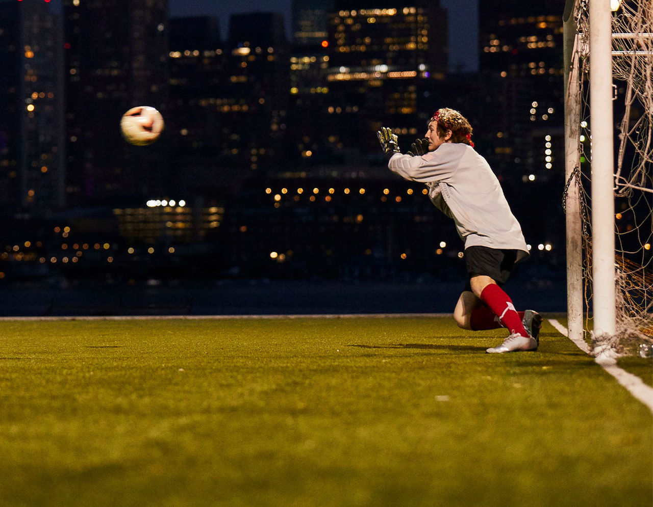 male goalie on field catching soccer ball at night