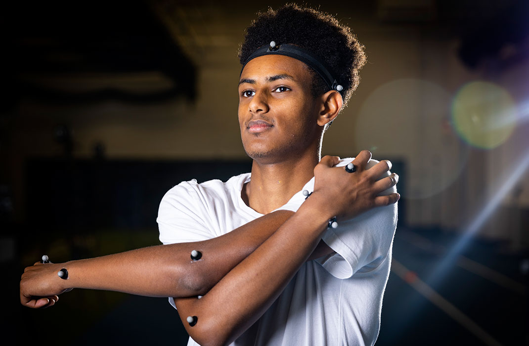 male athlete stretching his arm in sports facility with sensors attached on arms and head