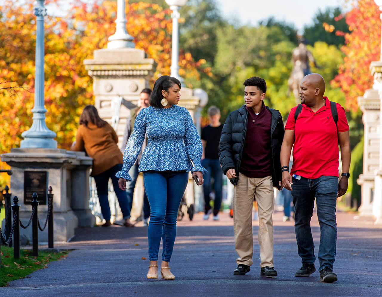 Latino parents and their teenaged son in Boston Public Garden, with autumn trees in the background.