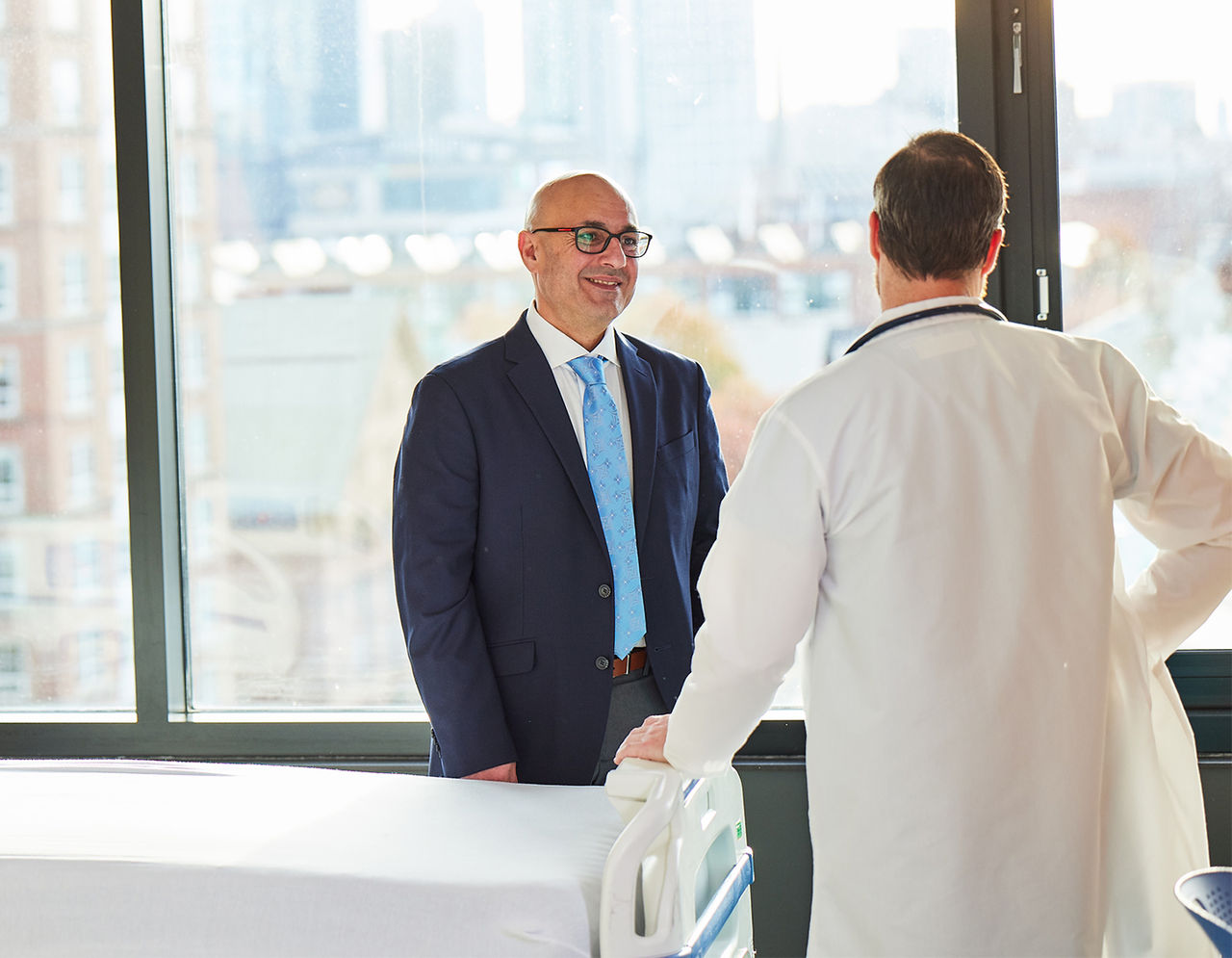 Suited man talking to doctor by patient bed